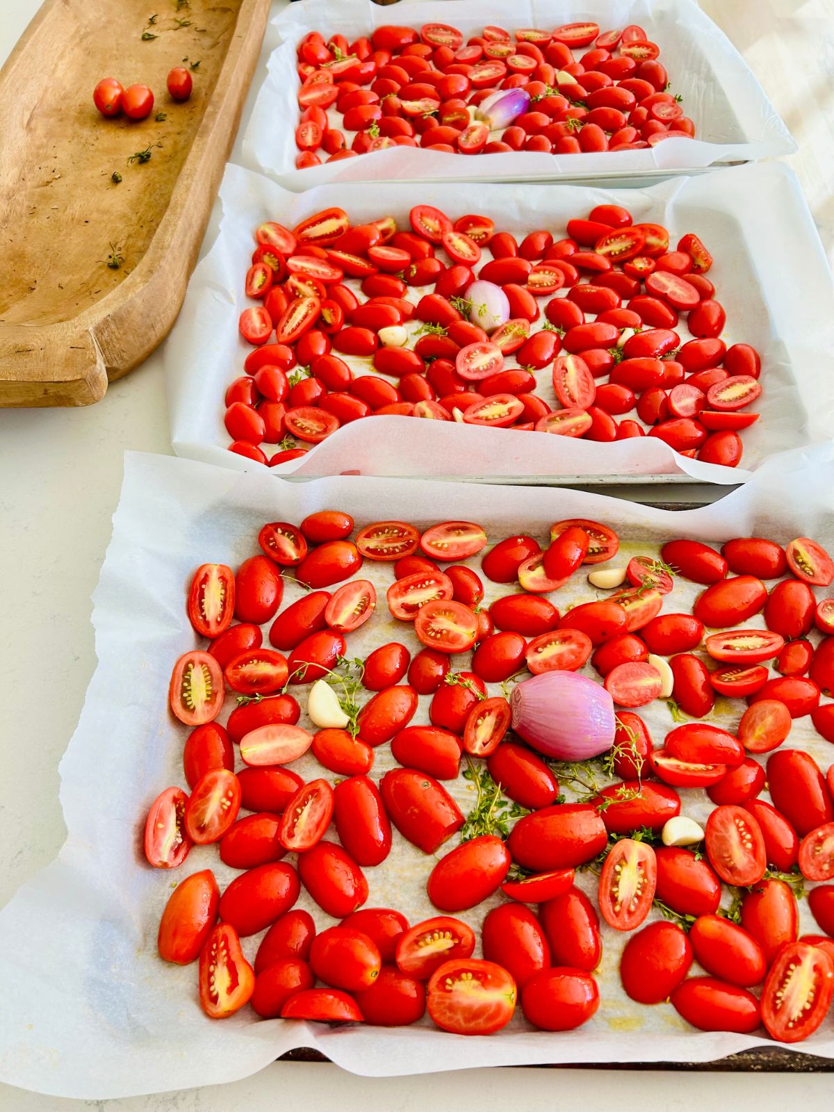 Three parchment-lined sheet pans loaded with fresh tomatoes, shallot, and garlic for this tomato paste recipe.