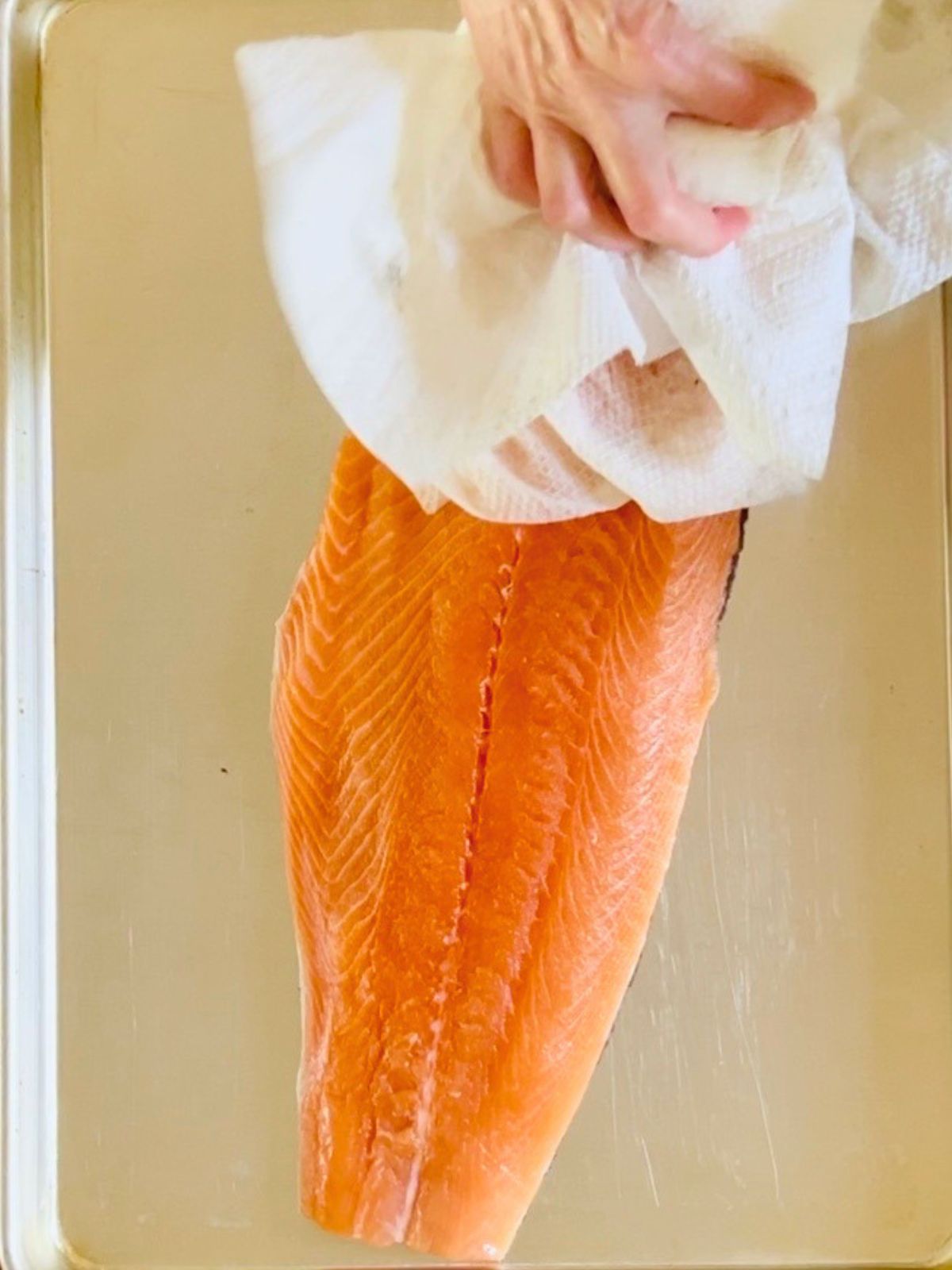 Brined salmon on a cookie sheet is patted dry with paper towels.