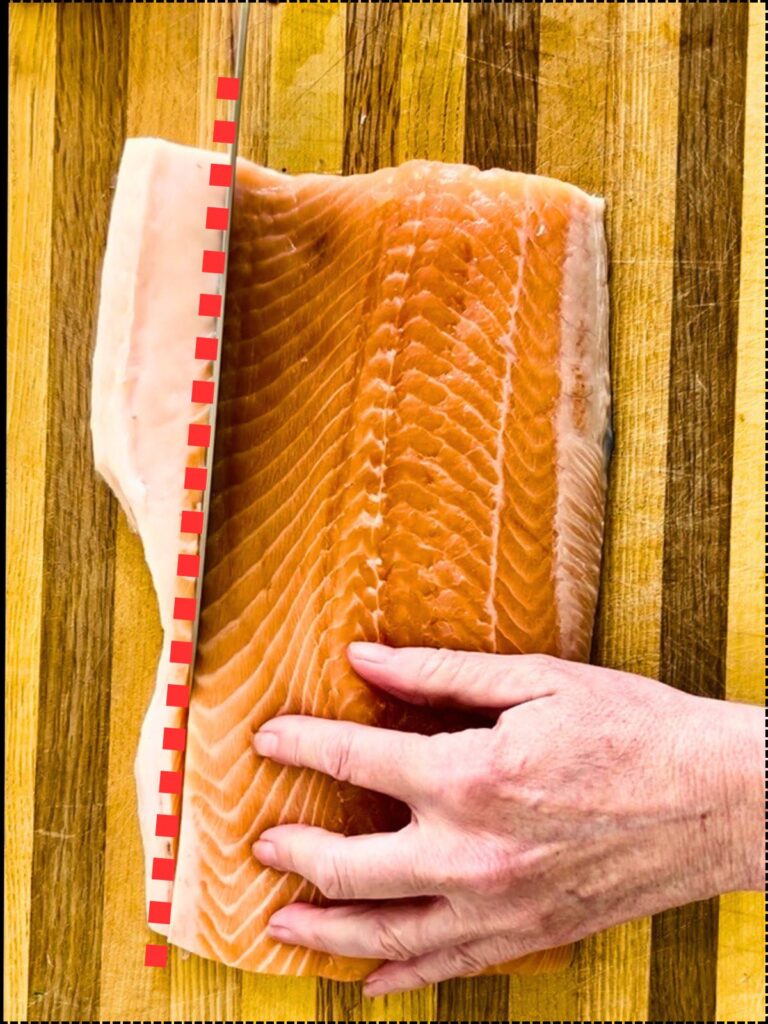 A full side of salmon on a cutting board with a red dotted line showing where to trim with a knife.
