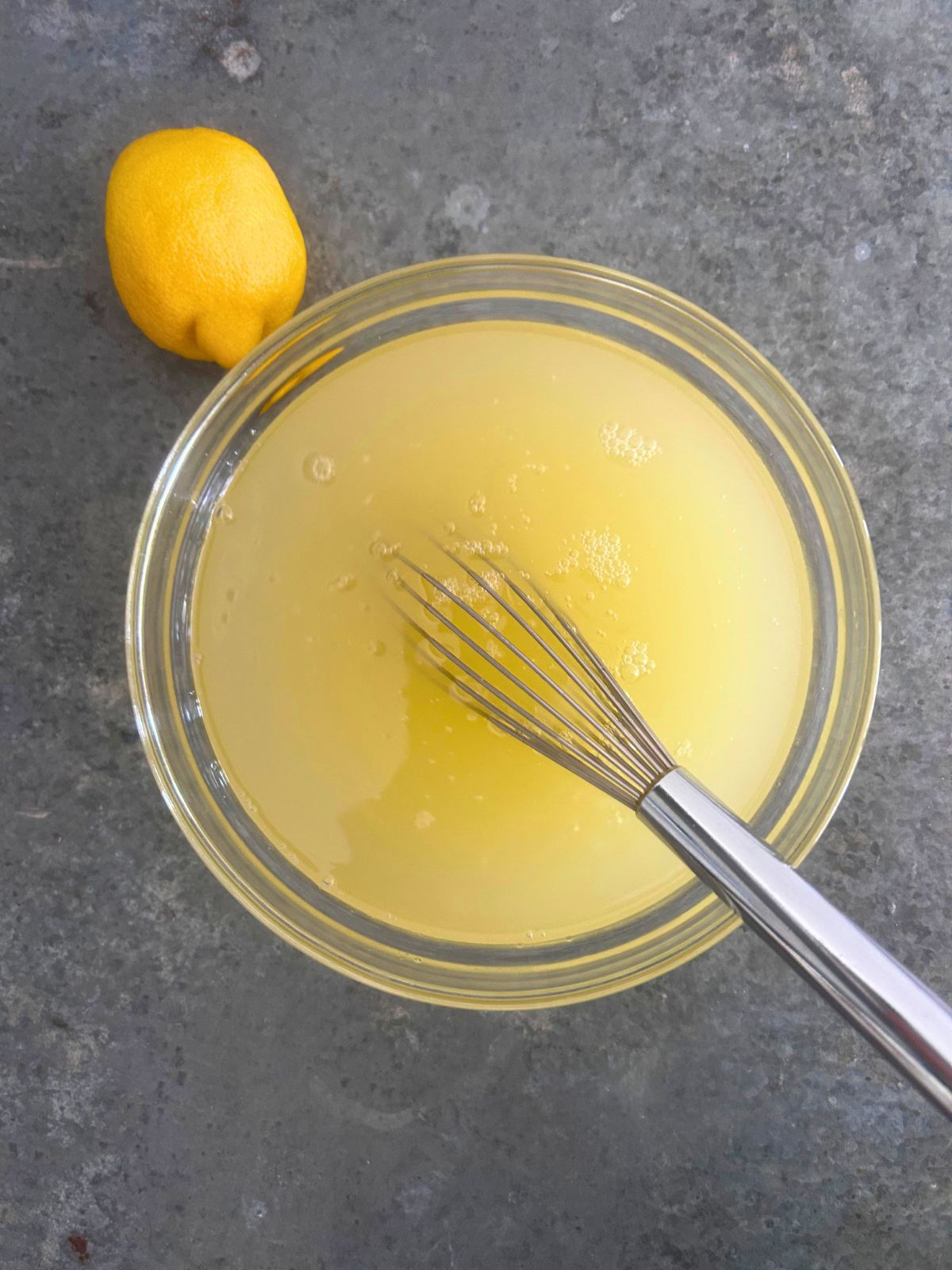Fresh lemon juice and sugar whisked in a glass bowl next to a lemon.