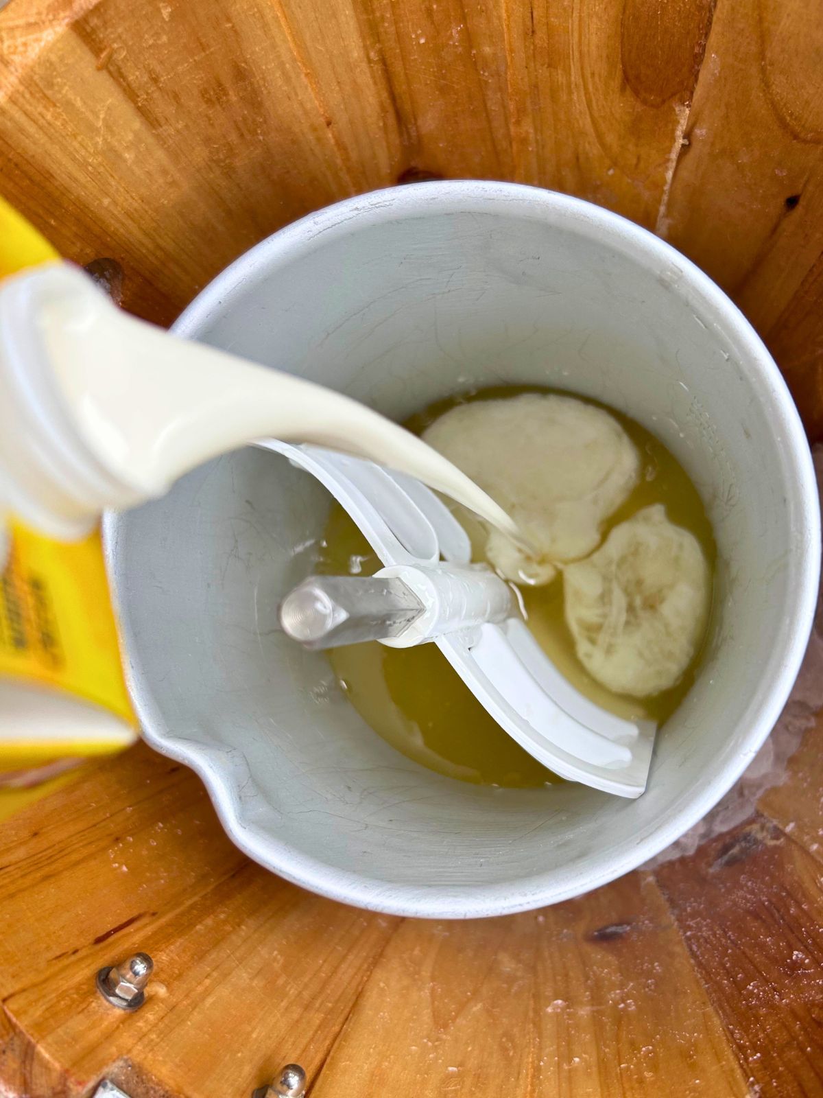 Cream is pouring into the lemon mixture inside the ice cream maker with a paddle ready to churn.