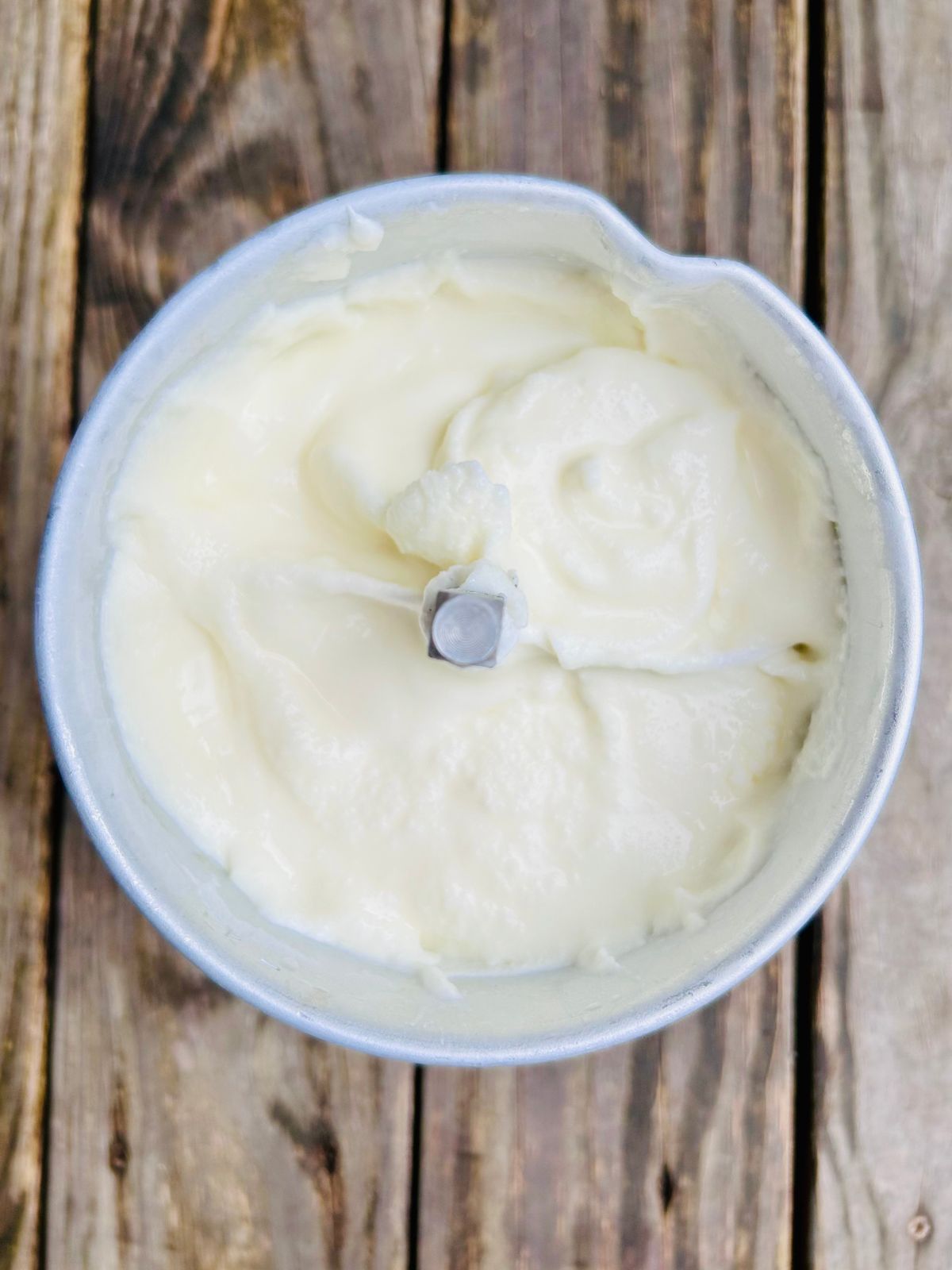 Churned lemon ice cream in an ice cream maker container with the paddle in it.