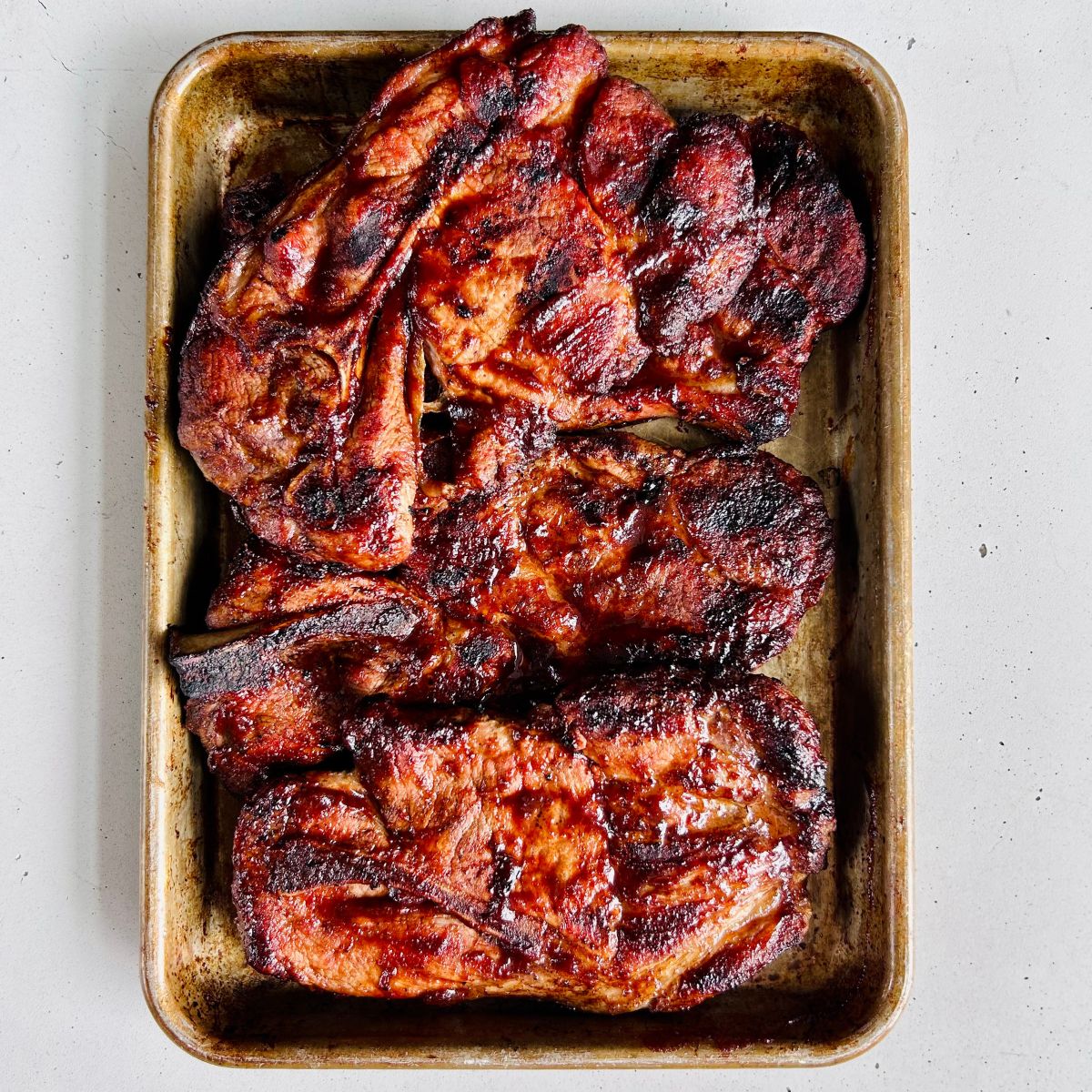Four grilled BBQ pork steaks on a cookie sheet.