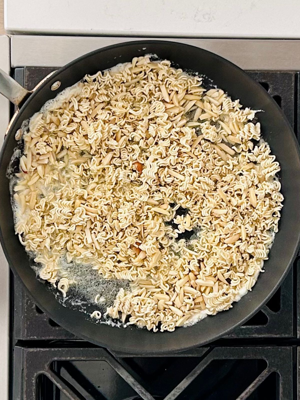 A skillet with melted butter slivered almonds and ramen noodles.