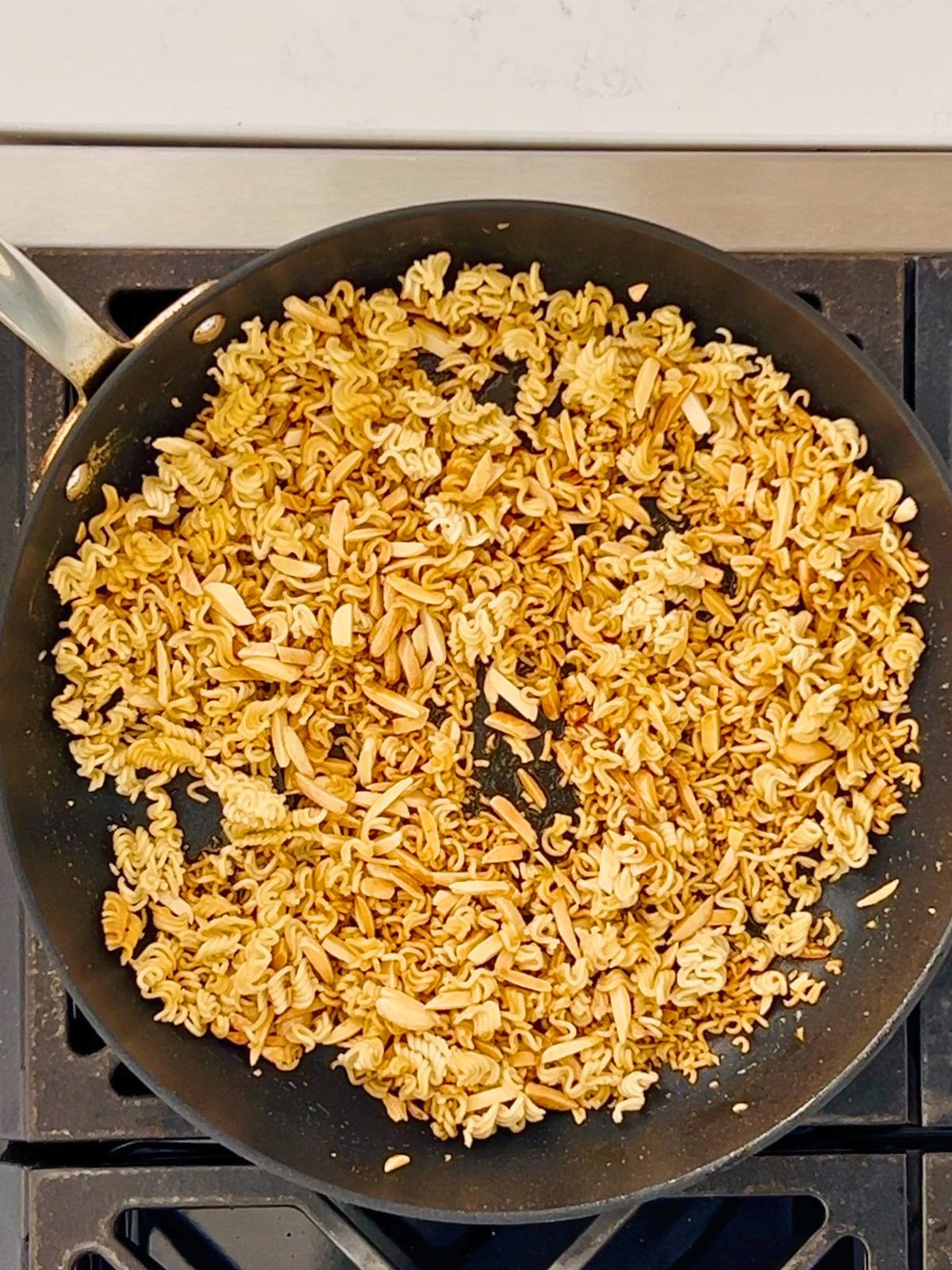 Toasted crushed ramen noodles and slivered almonds in a skillet.