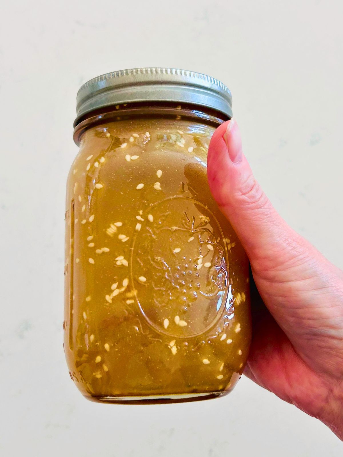 A mason jar with mixed Asian salad dressing with sesame seeds for crunchy romaine salad.