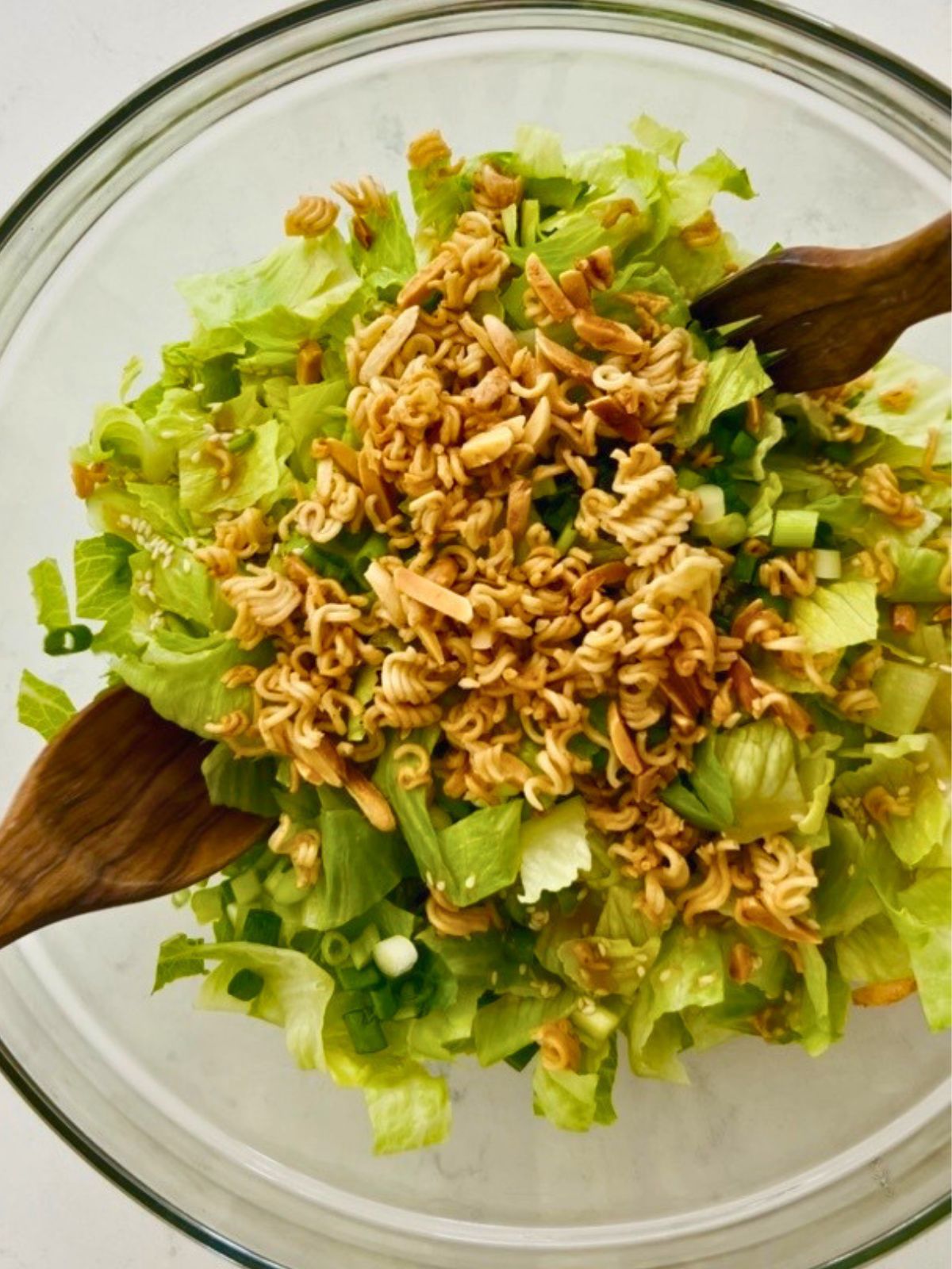 Wooden salad utensils are tossing a glass bowl of crunchy romaine salad.