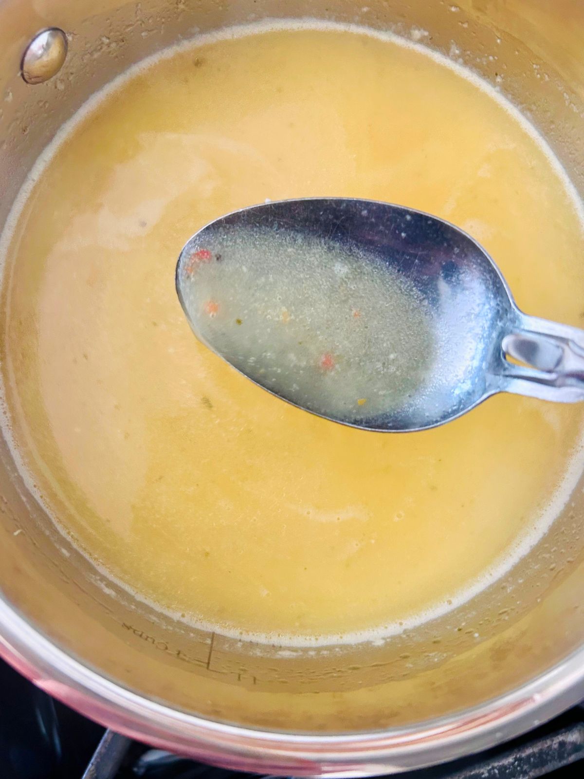 A spoonful of butter, vinegar, beer, and Italian seasoning is held over the pot of sauce.