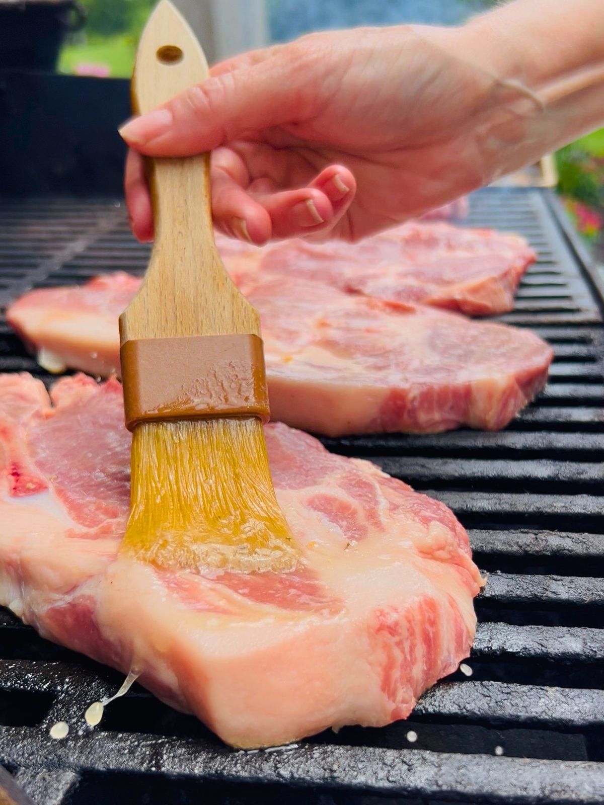 BBQ pork steaks are getting basted with butter and vinegar as soon as they placed on the grill.