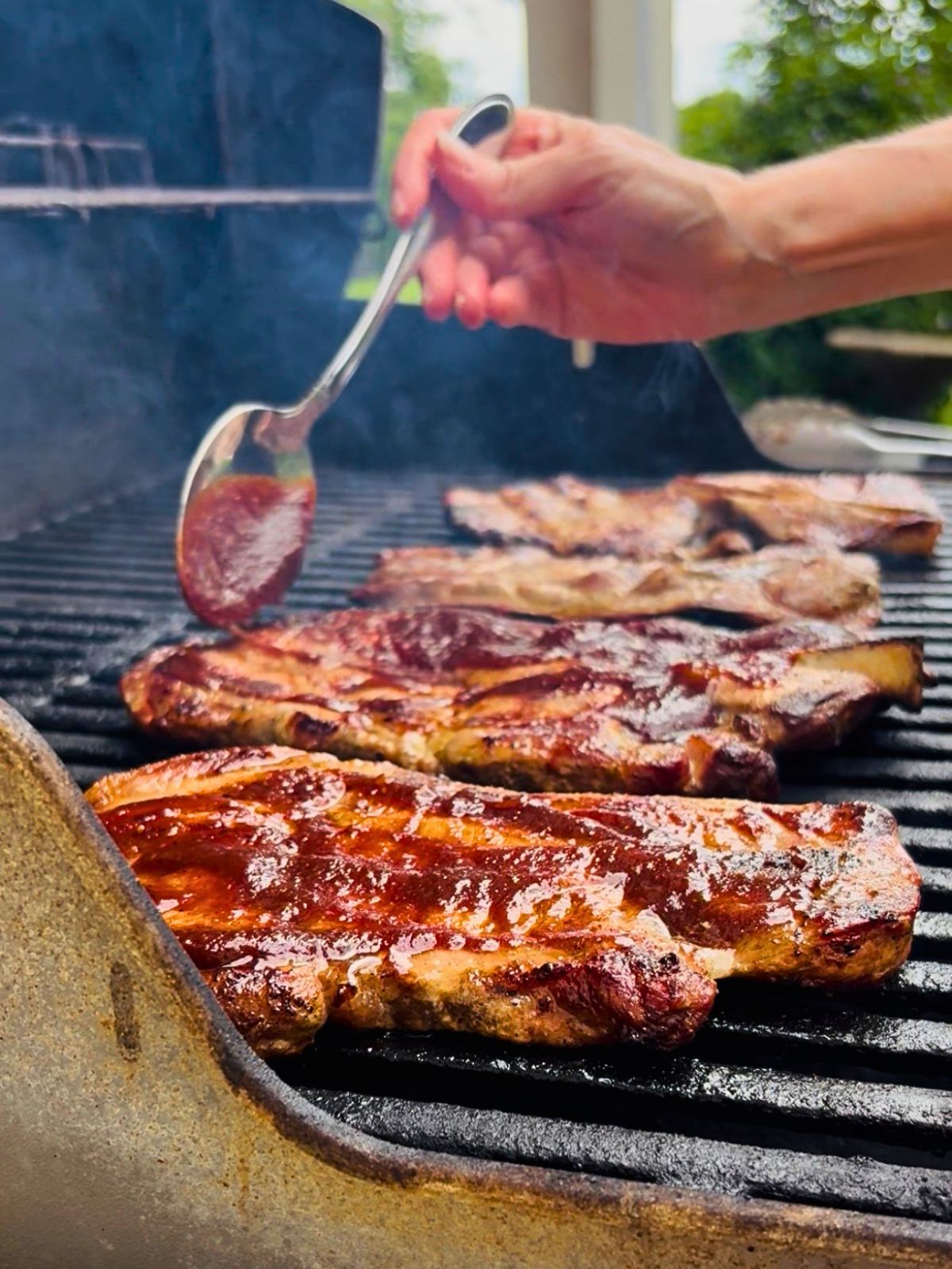 Barbecue sauce is spooned over pork steaks on the grill.
