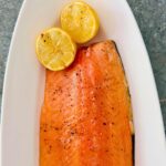 Easy grilled side of salmon on a Traeger on a white oval platter with 2 lemon halves.