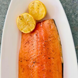 Easy grilled side of salmon on a Traeger on a white oval platter with 2 lemon halves.