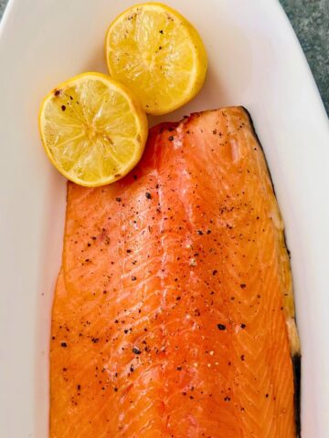 Easy grilled side of salmon on a Traeger on a white oval platter with 2 lemon halves.