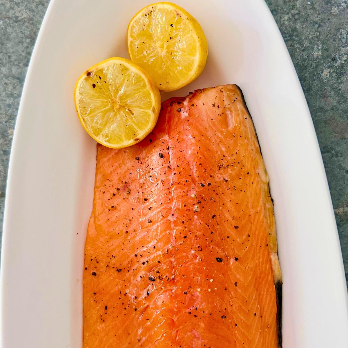 Easy grilled side of salmon on a Traeger on a white oval platter with 2 lemon halves.