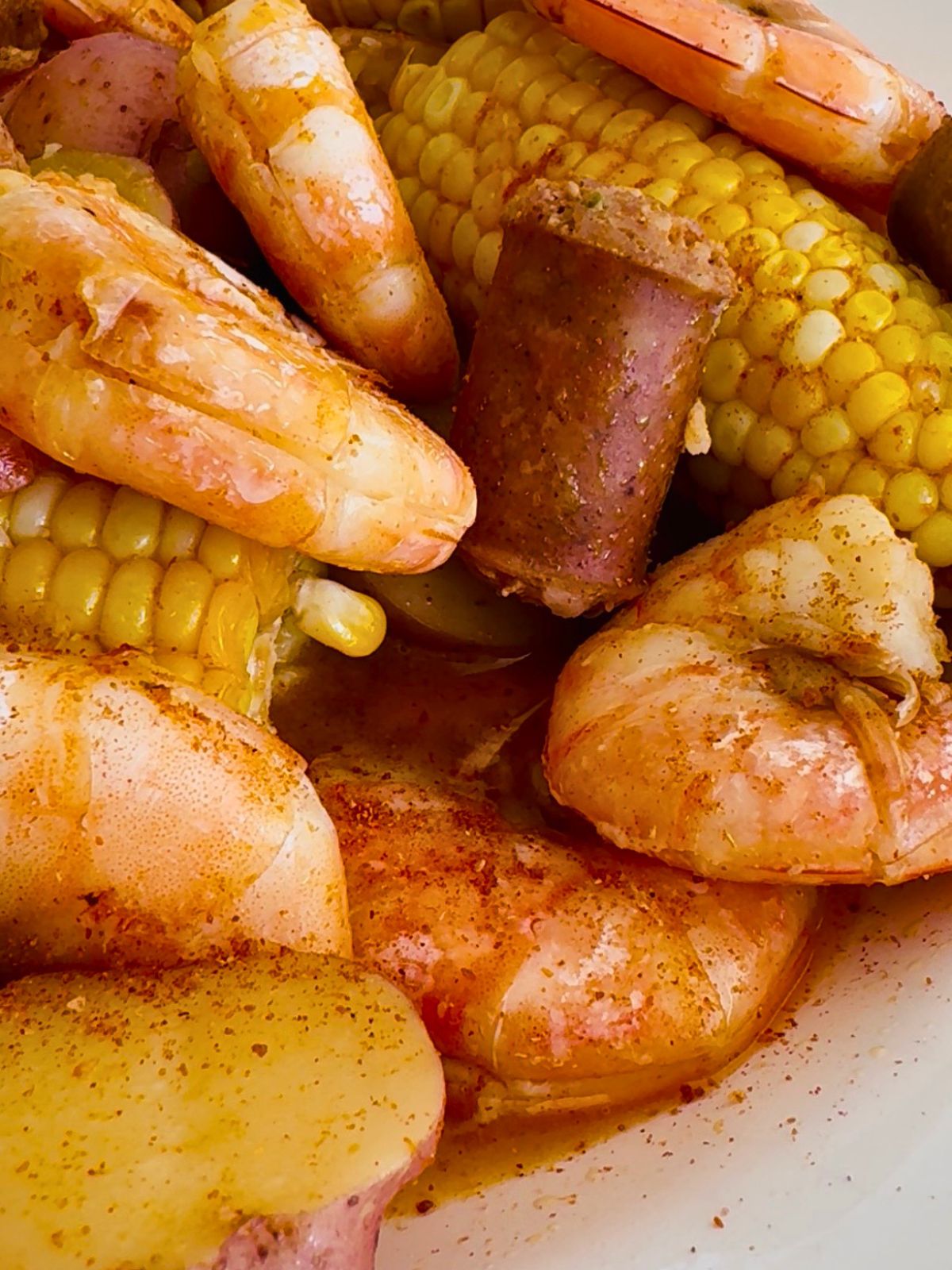 Close-up of seasoned shrimp, corn, sausage and their juices from an oven-baked shrimp boil.