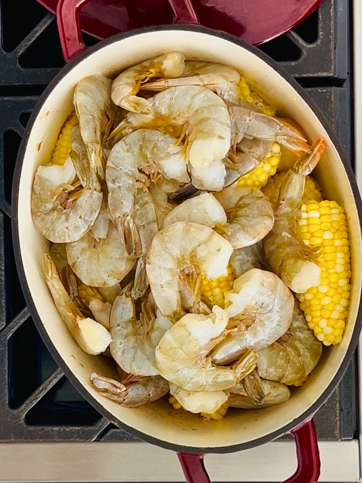 Raw shrimp added to corn and broth, cooking together for an oven-baked shrimp boil.