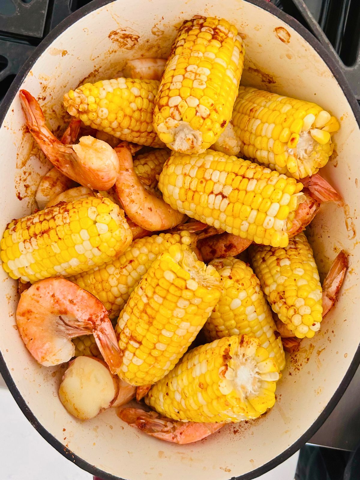 Cooked shrimp, corn, and potatoes seasoned and ready in a Dutch oven baked shrimp boil.