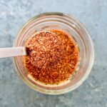 A teaspoon of taco seasoning with tomato powder held over a small mason jar of seasoning.