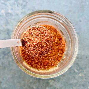 A teaspoon of taco seasoning with tomato powder held over a small mason jar of seasoning.