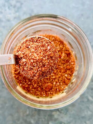 A teaspoon of taco seasoning with tomato powder held over a small mason jar of seasoning.