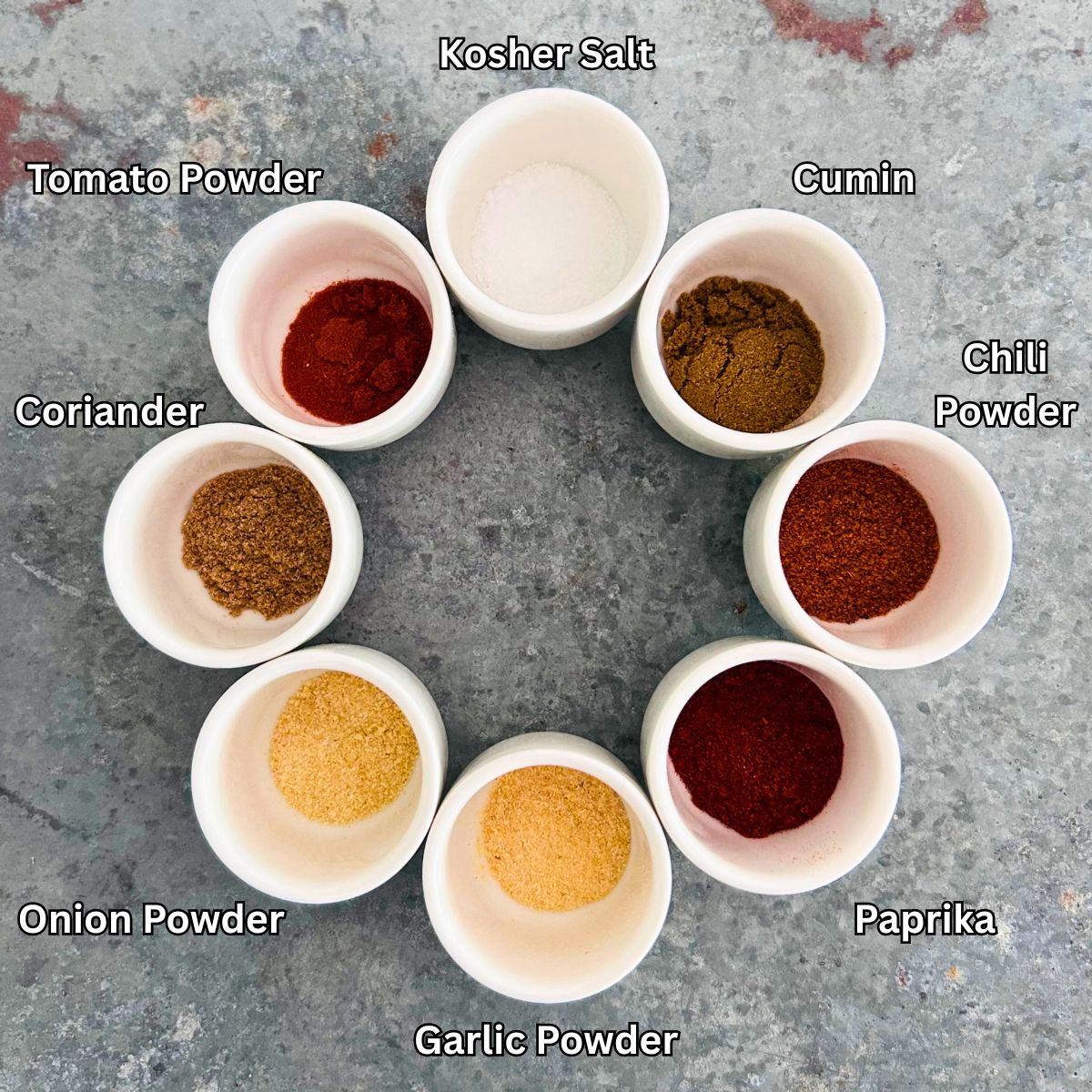 Eight ingredients for taco seasoning recipe with tomato powder in individual white sake cups.