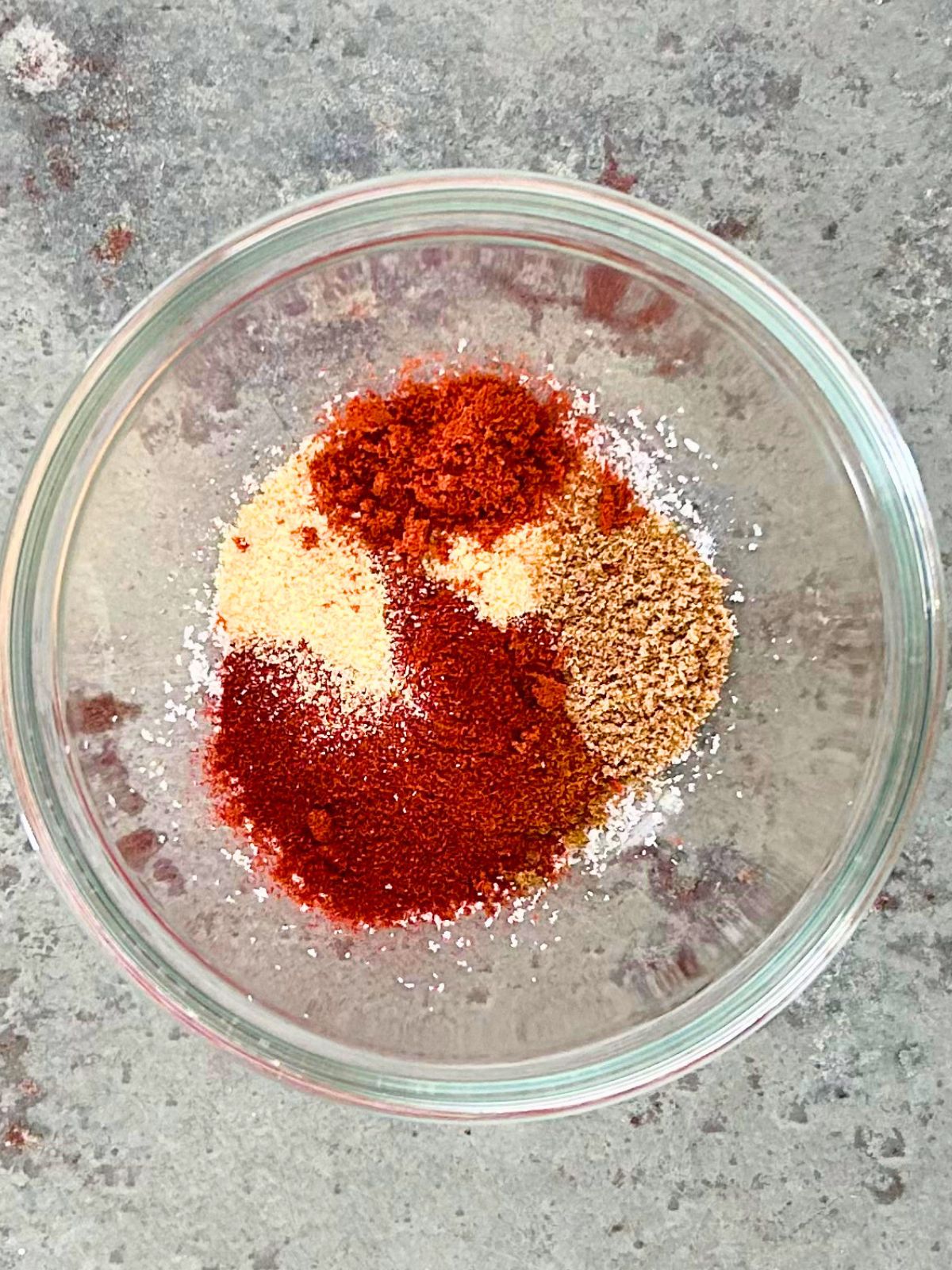 Chili, garlic, onion, tomato, and coriander powders are added to kosher salt for taco seasoning in a small glass bowl.