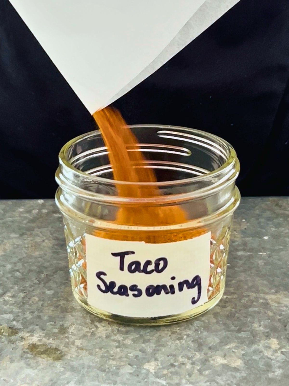 Parchment paper is used to funnel taco seasoning into a small mason jar for storage.