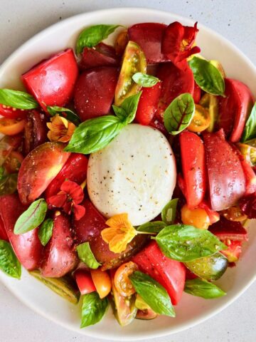 Burrata and heirloom tomato salad with basil and edible flowers on a white plate.