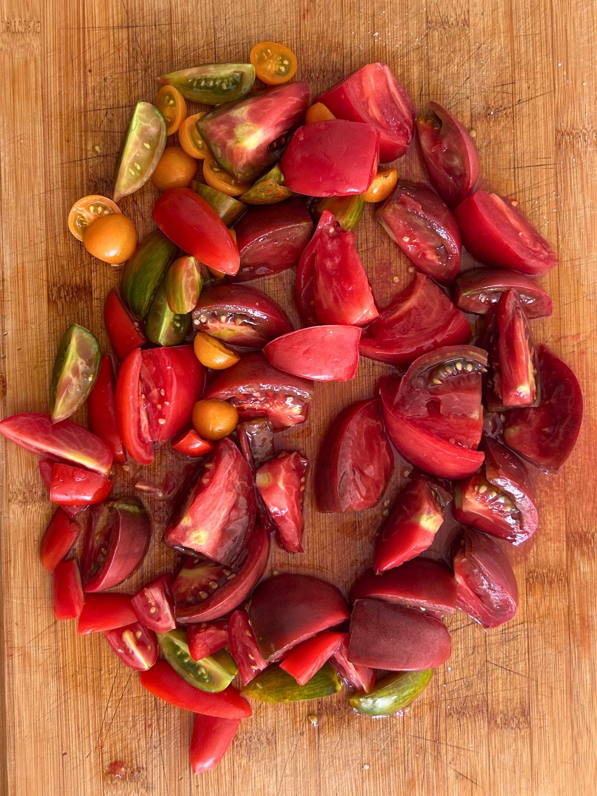 Bite size pieces of salted garden tomatoes and their juices resting on a cutting board.