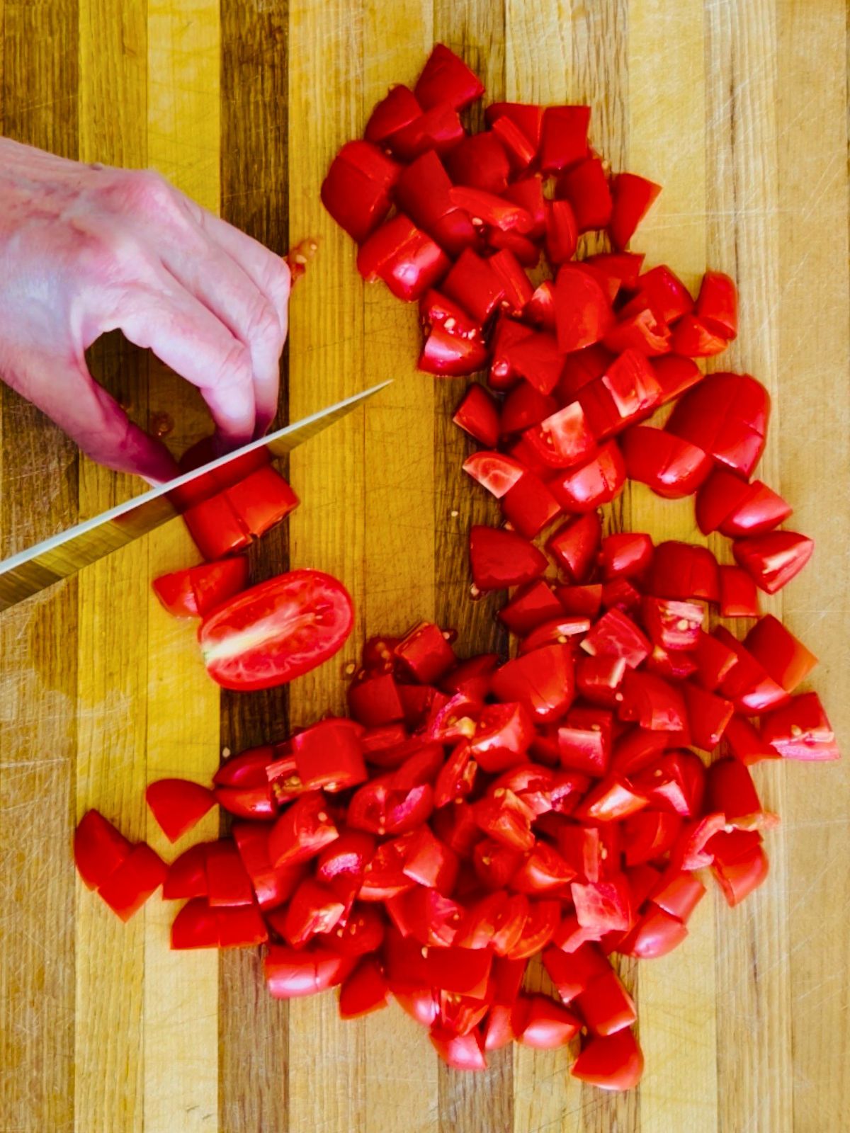 Red cherry tomatoes are diced into small pieces on a cutting board.