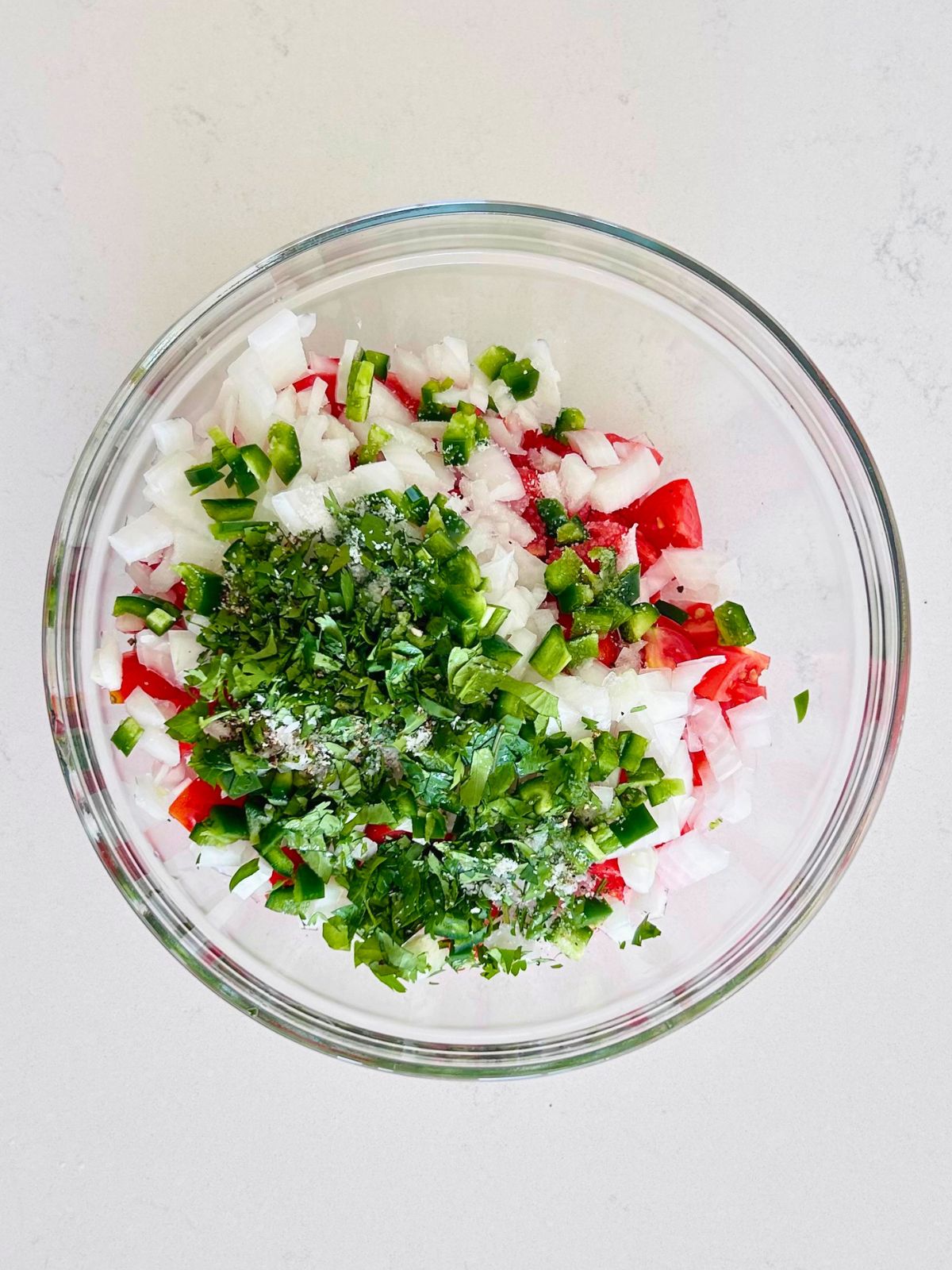 Chopped tomatoes, white onion, jalapeño, cilantro, and salt in a glass bowl for pico de gallo.