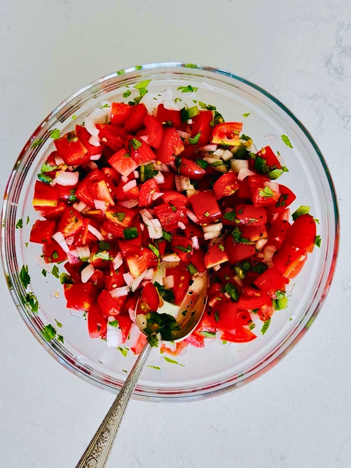 Pico de gallo with cherry tomatoes in a glass bowl with a spoon.