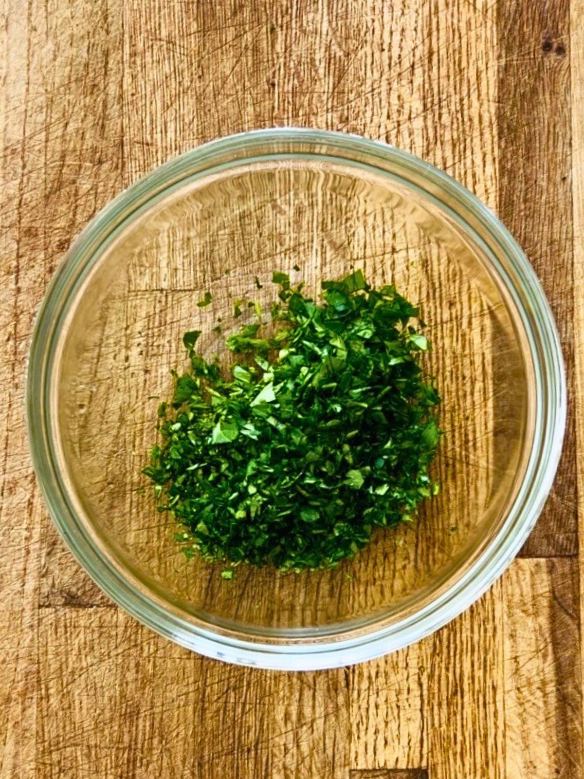 A glass bowl holding finely chopped cilantro and parsley.