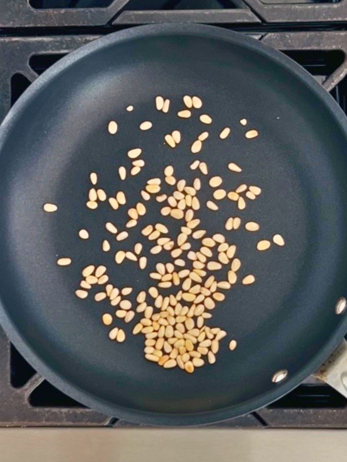 Pine nuts are toasting in a dry skillet over a burner.