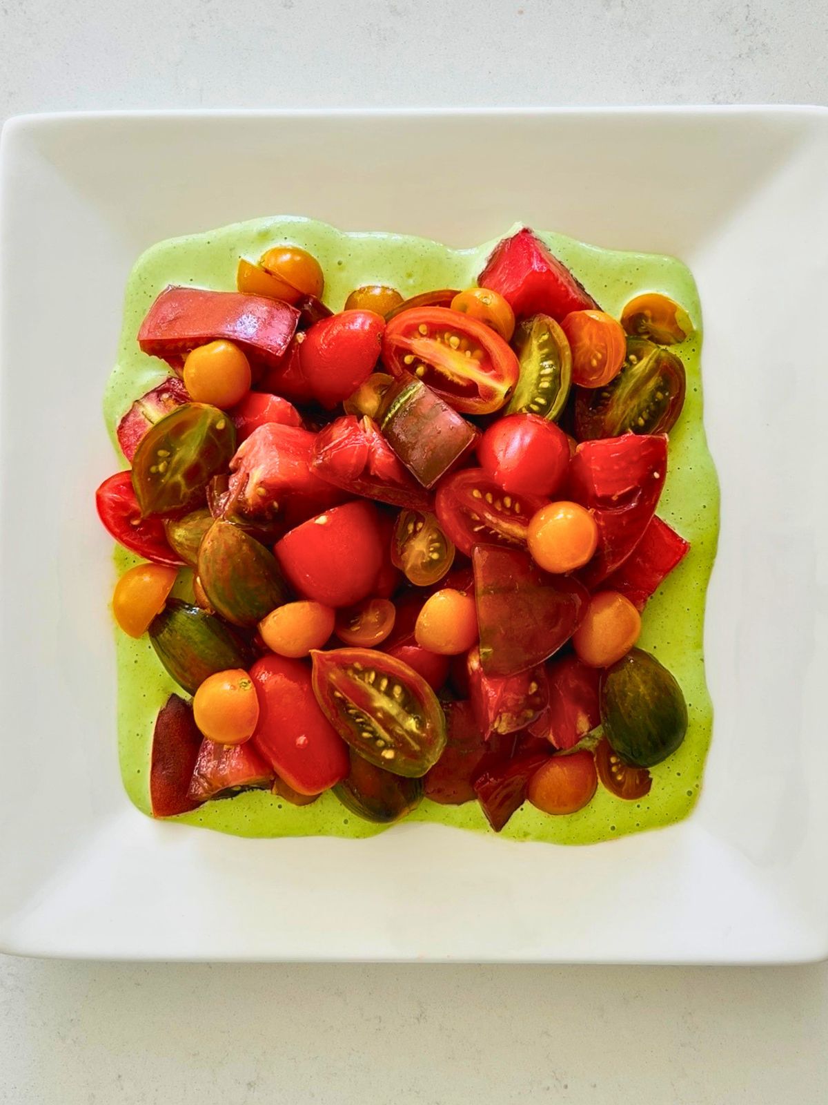 A white plate with heirloom tomatoes resting over a pool of green goddess dressing.