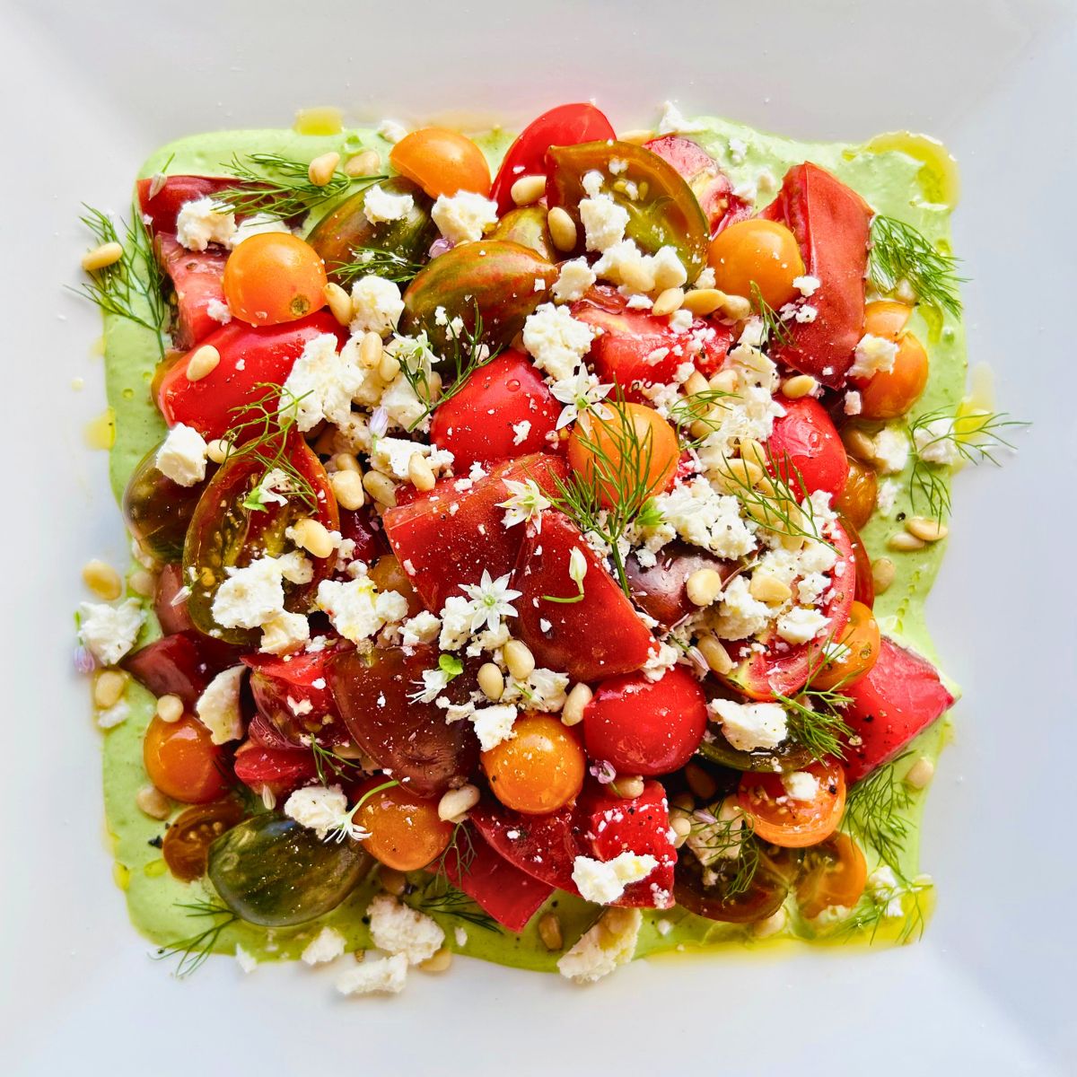 A white plate with fresh tomato salad with feta, pine nuts, dill, and green goddess dressing.