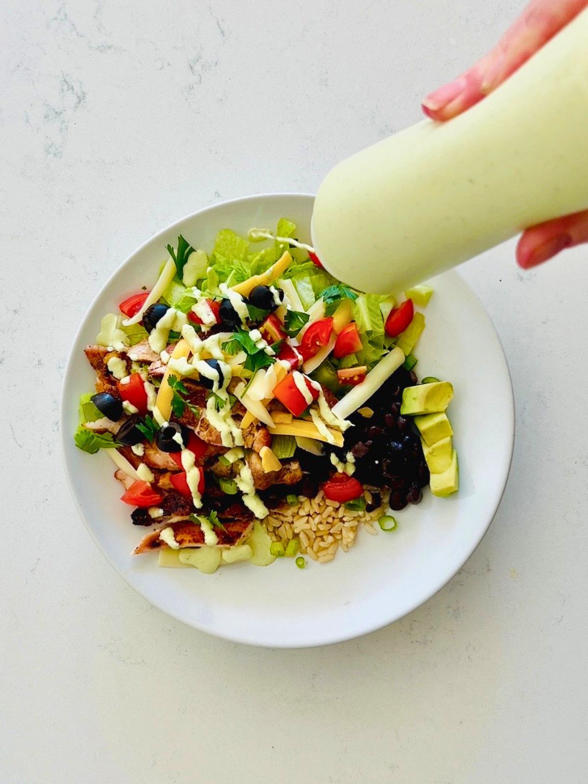 Chicken burrito bowls are drizzled with jalapeño ranch dressing in a squeeze bottle.