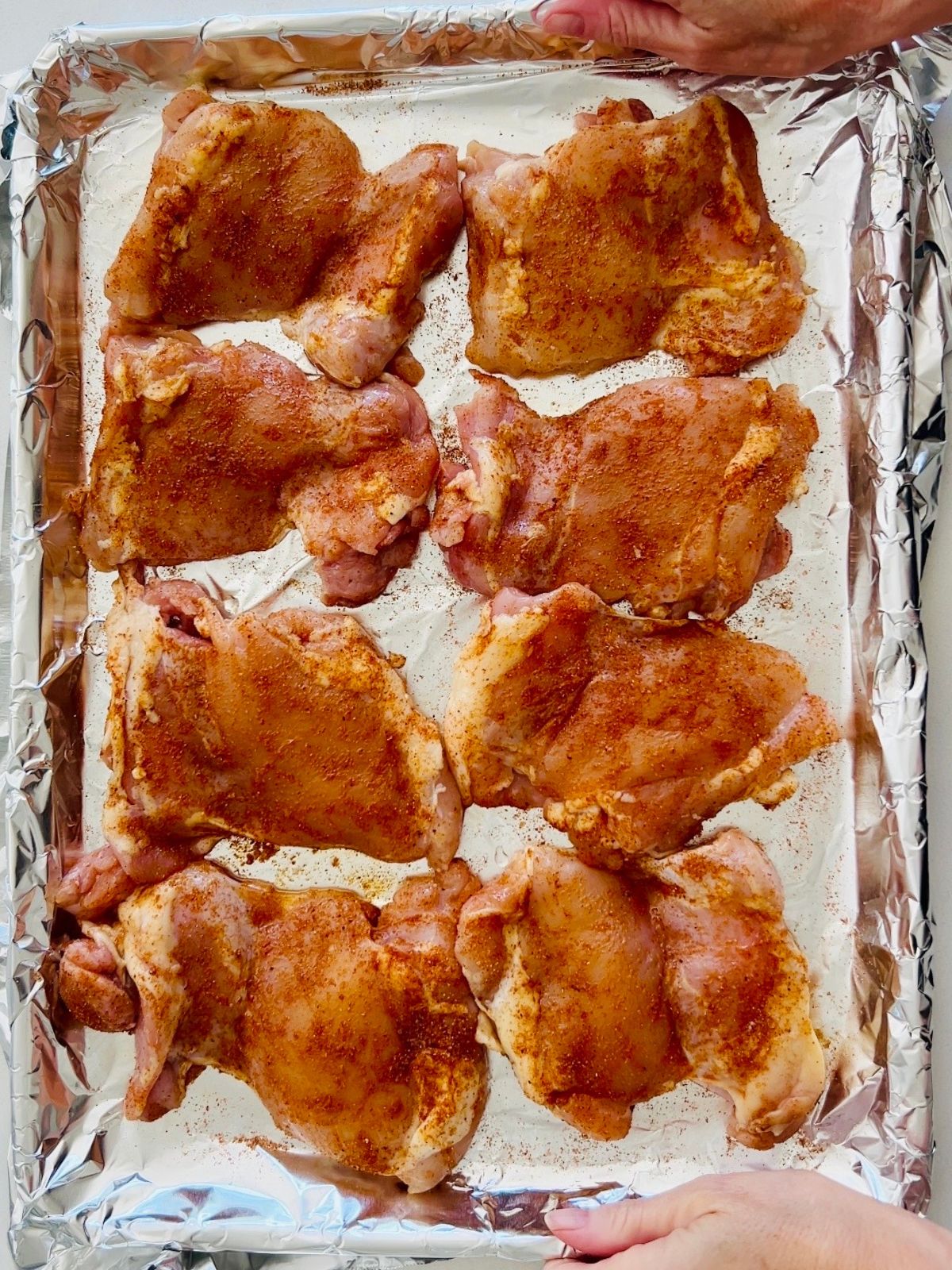 Seasoned and oiled boneless, skinless chicken thighs arranged on a foil-lined rimmed baking sheet.