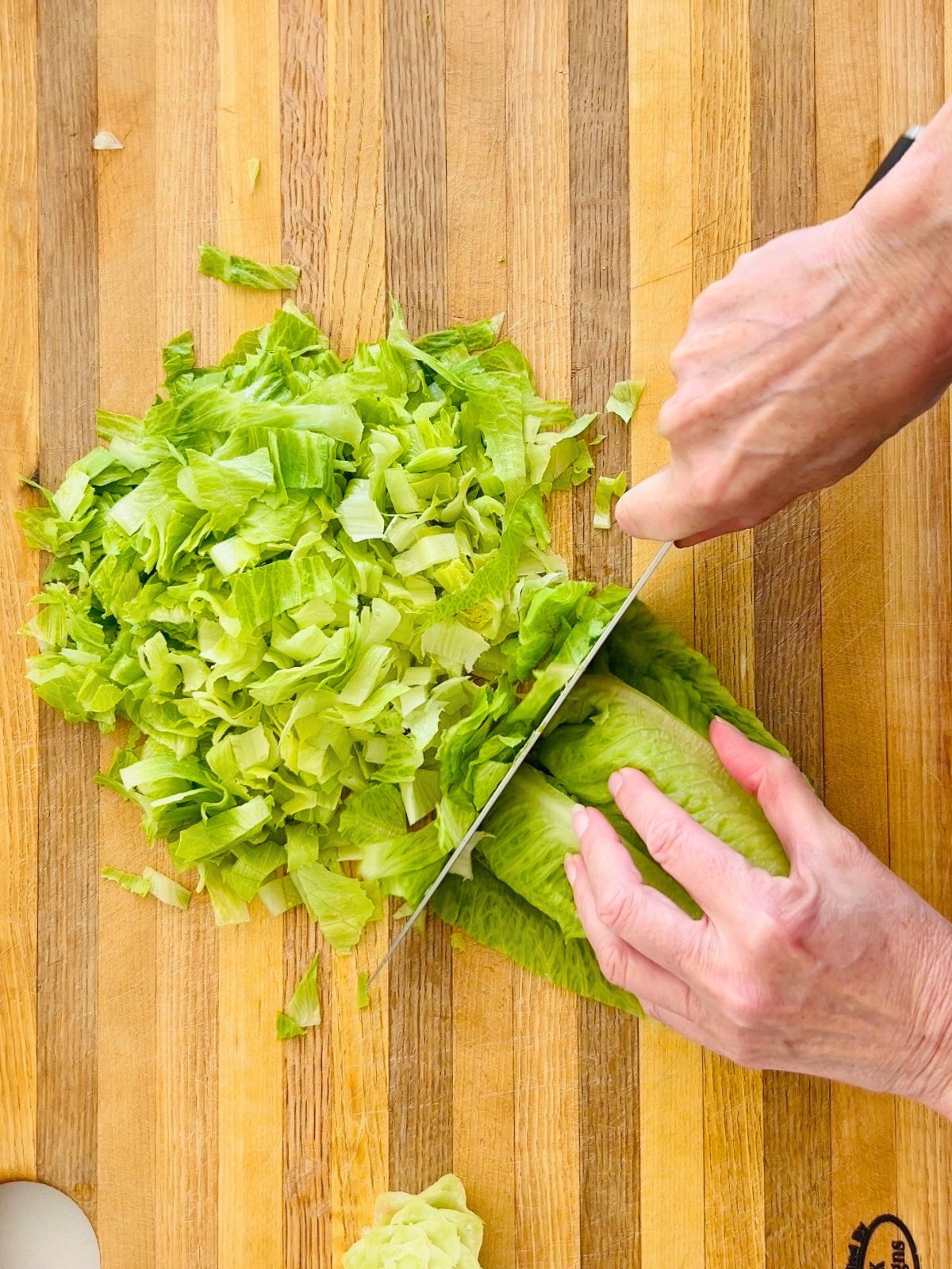 A romaine heart is getting chopped with a butcher's knife over a wooden cutting board.
