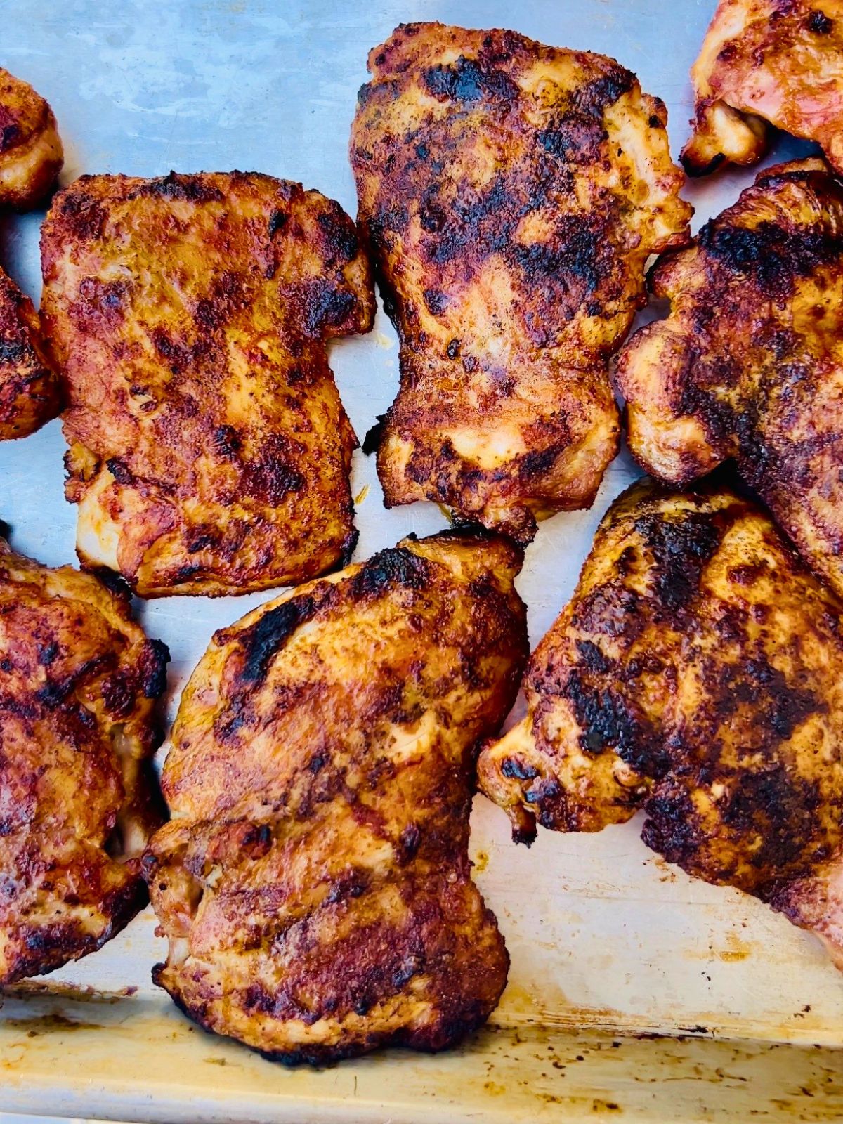 Seasoned and grilled boneless skinless chicken thighs resting on a rimmed baking sheet.