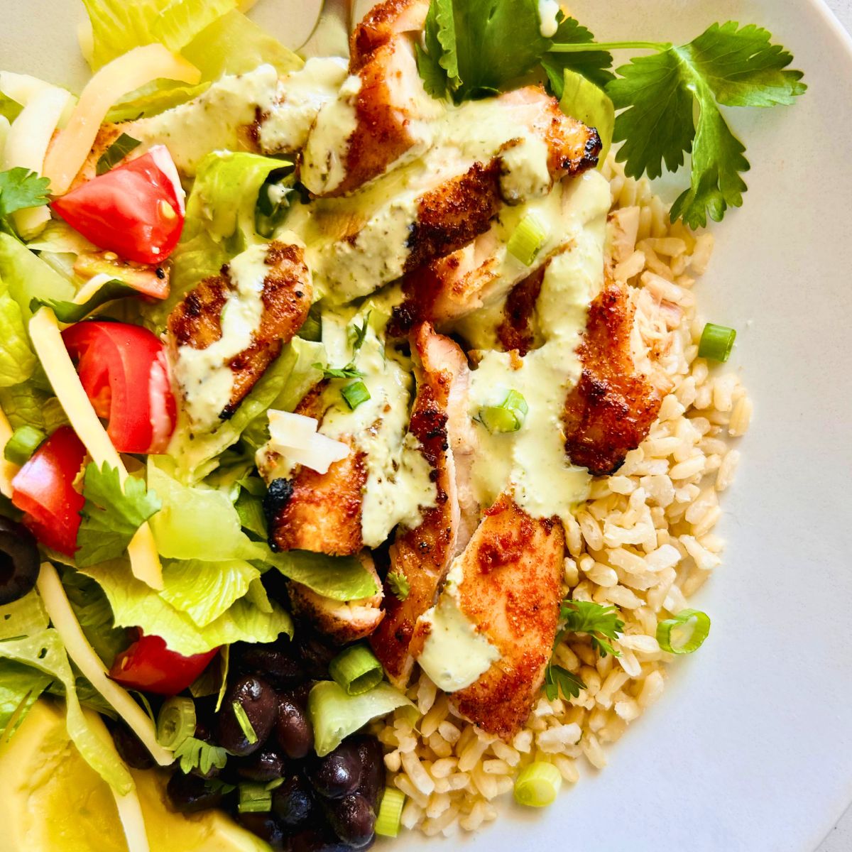 Chicken Burrito Bowls With Jalapeño Ranch drizzled on top with rice, black beans, and romaine lettuce.