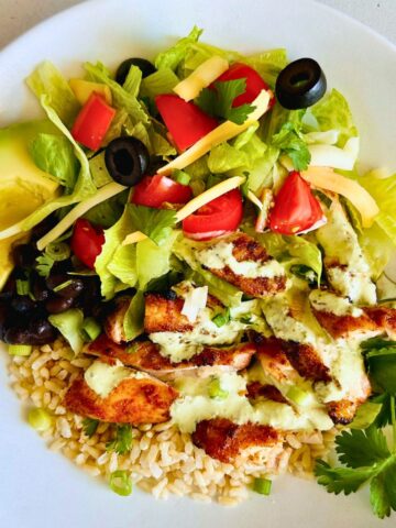 Chicken burrito bowls with jalapeño ranch and fresh toppings with a fork nestled on a white plate.