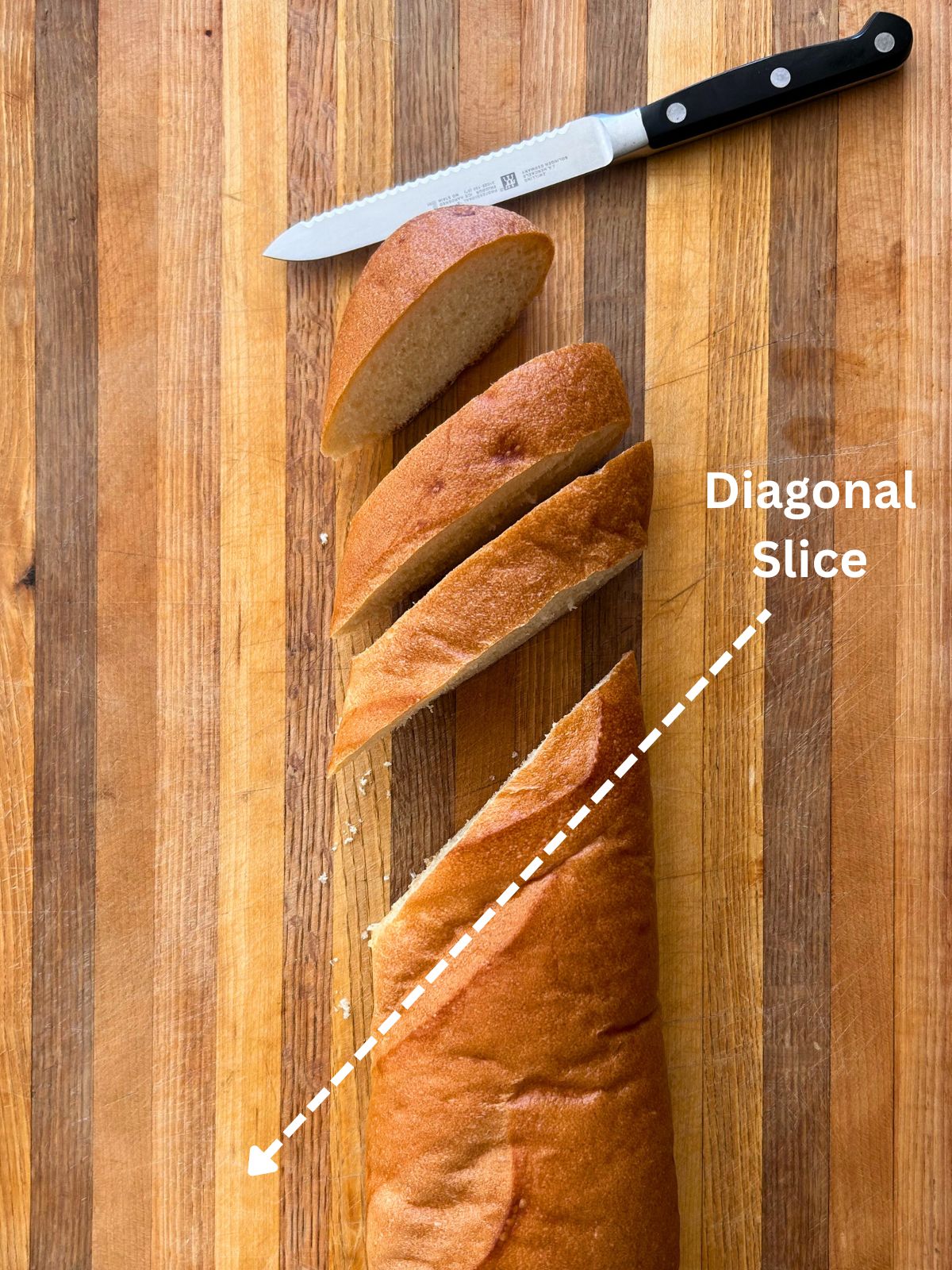 French bread and a bread knife on a cutting board with an arrow showing where to cut diagonal slices on the loaf.