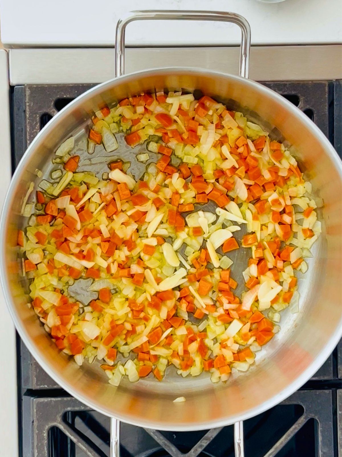 A large pot with chopped onions, carrots, and garlic cooking in butter.