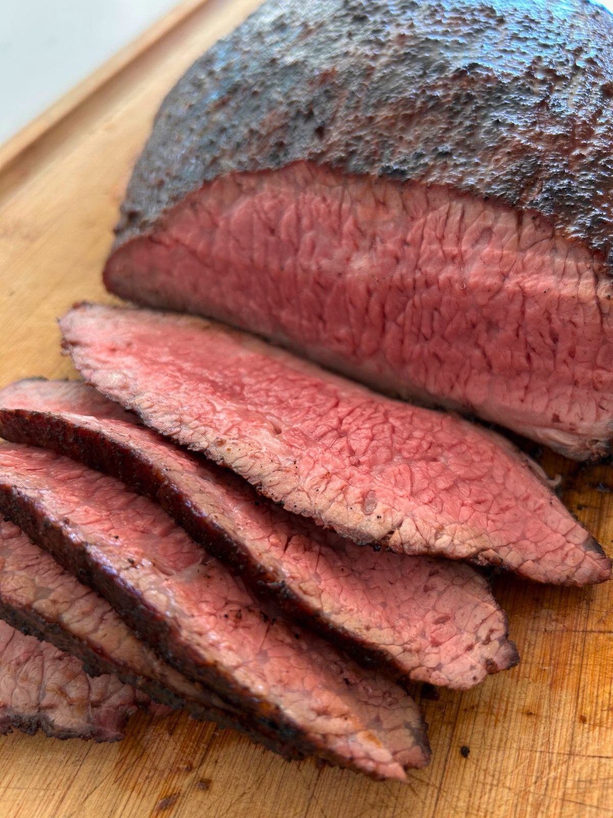Sliced, medium cooked flank steak on a cutting board for open-faced steak sandwiches.