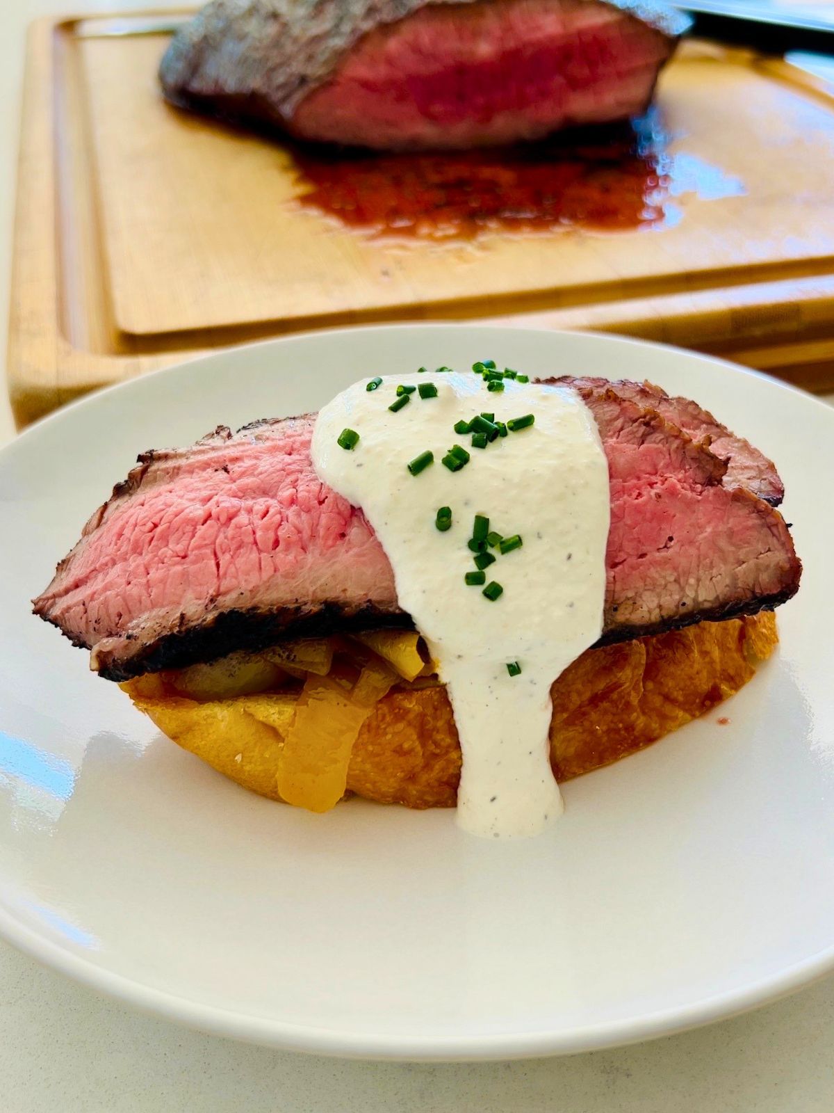 Open-faced steak sandwich with sliced flank steak, caramelized onions, and creamy horseradish on top of a piece of toasted French bread.