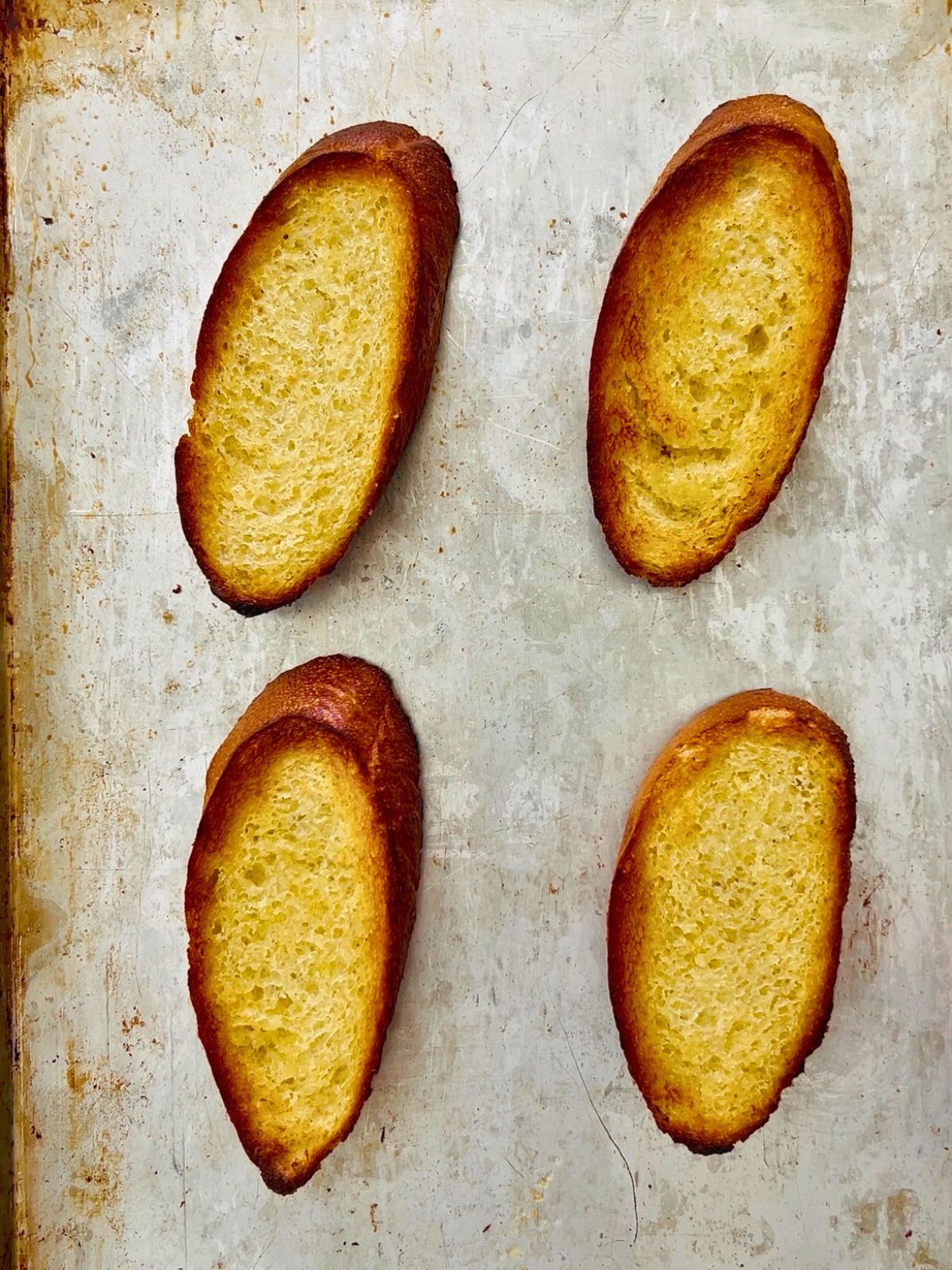 Four oblong buttered pieces of French bread toasted on a cookie sheet.