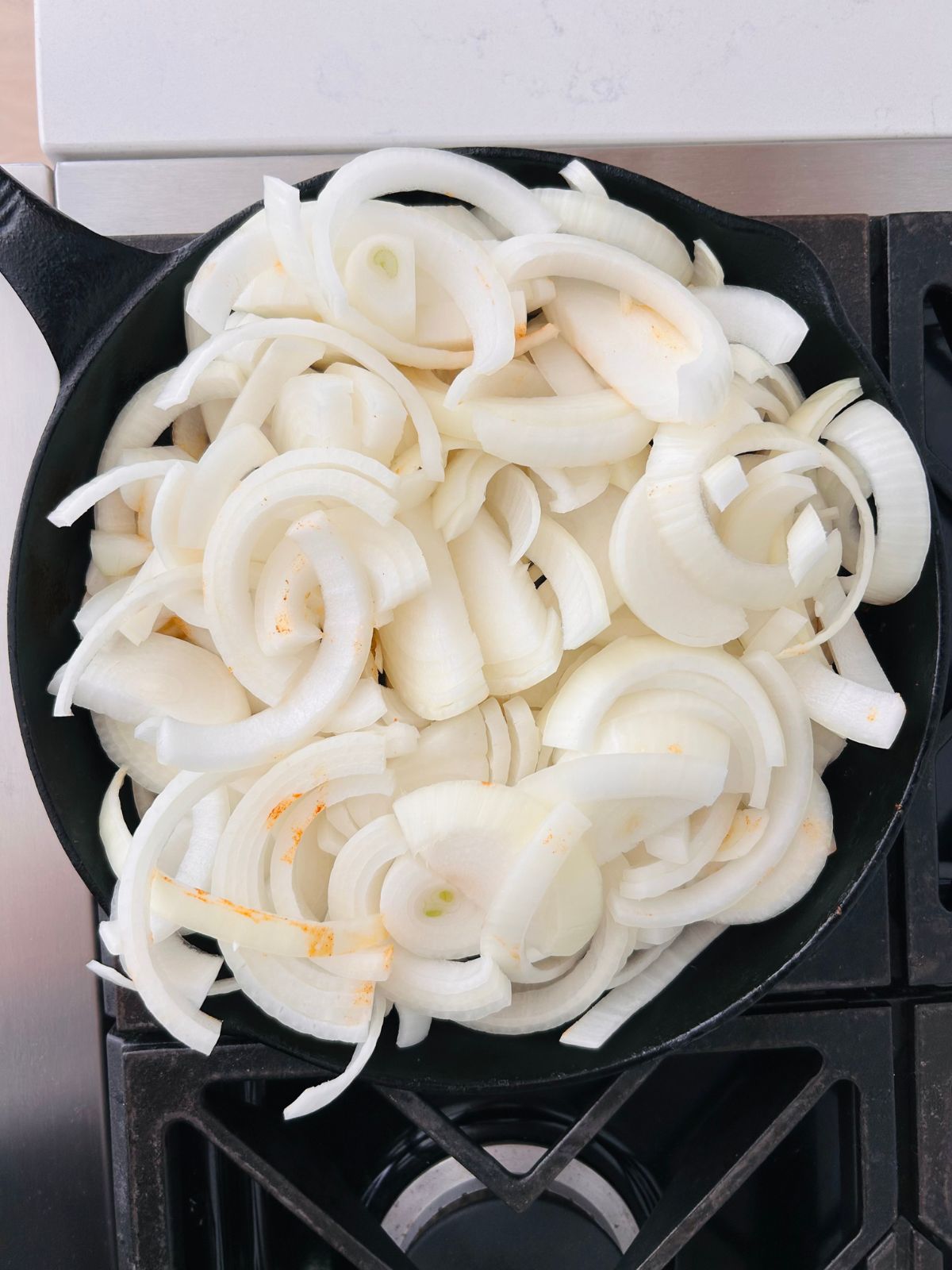 A large pile of sliced white onions starting to cook in a cast iron skillet.