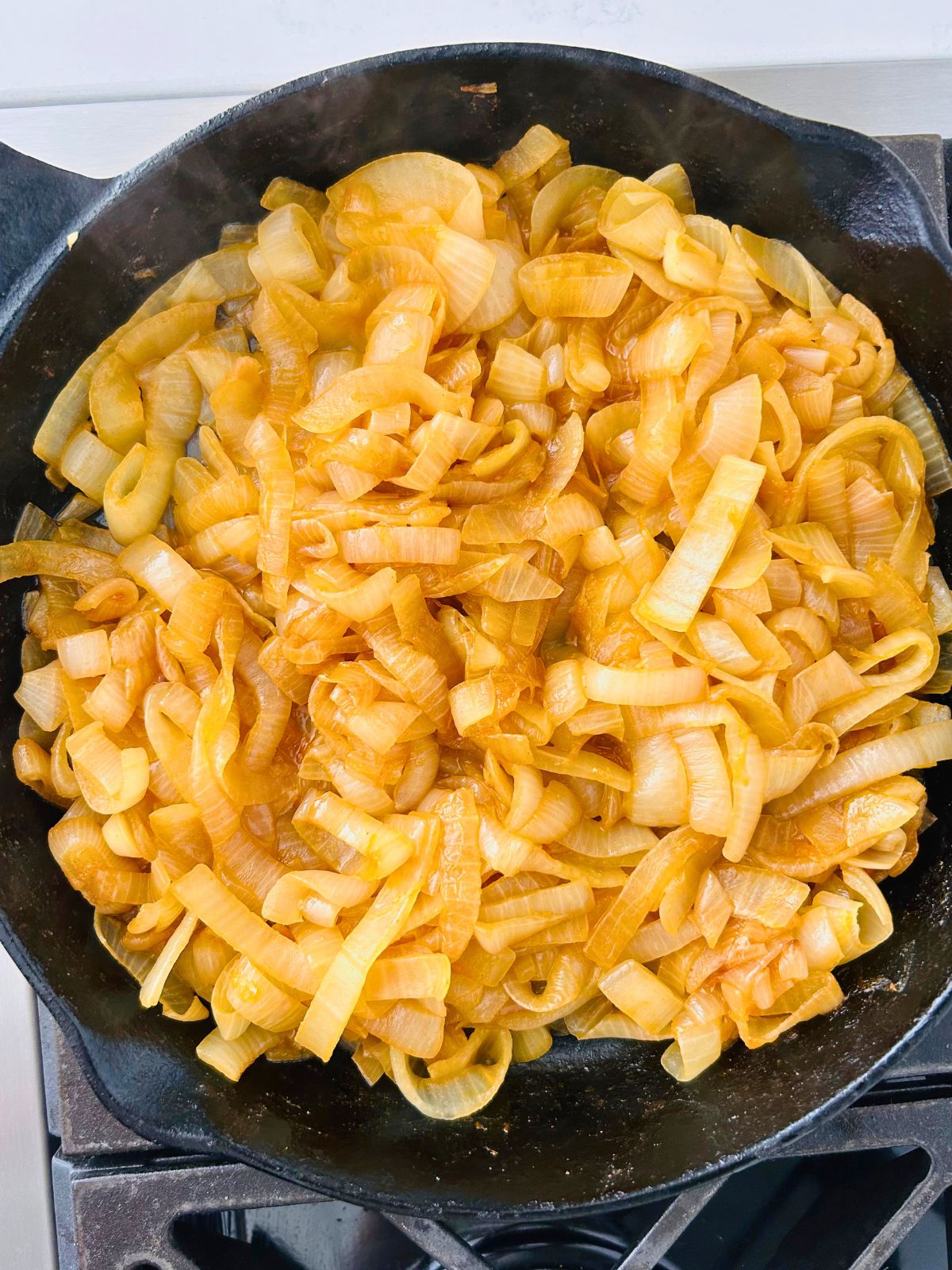 A cast iron skillet over a burner with caramelized onion in butter and paprika.