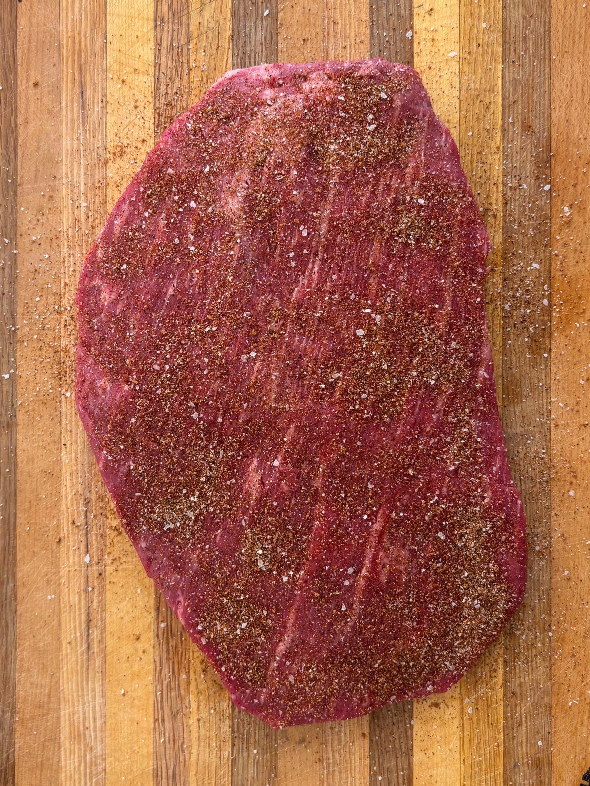 A cutting board with uncooked flank steak that has been generously seasoned with espresso rub.